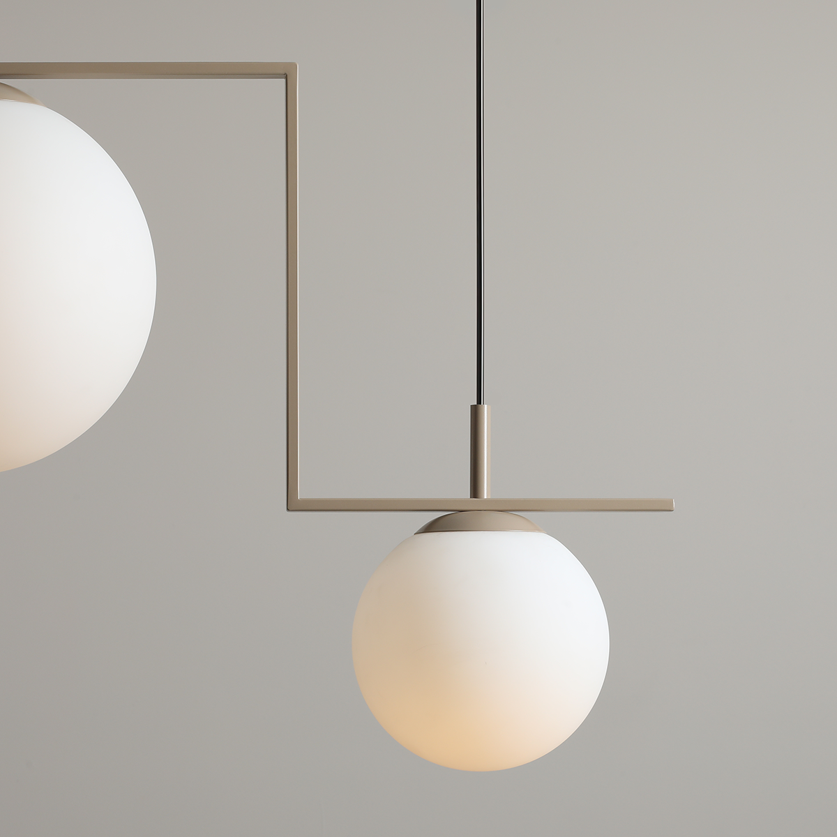 Beżowa lampa wisząca Zac II z dwoma oprawami E27, z prostą metalową konstrukcją. Lampa posiada białe, okrągłe klosze z matowego szkła, zawieszona na czarnym przewodzie. Ujęcie z boku, pokazujące detal i kształt kloszy.