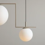 Beżowa lampa wisząca Zac II z dwoma oprawami E27, z prostą metalową konstrukcją. Lampa posiada białe, okrągłe klosze z matowego szkła, zawieszona na czarnym przewodzie. Ujęcie z boku, pokazujące detal i kształt kloszy.