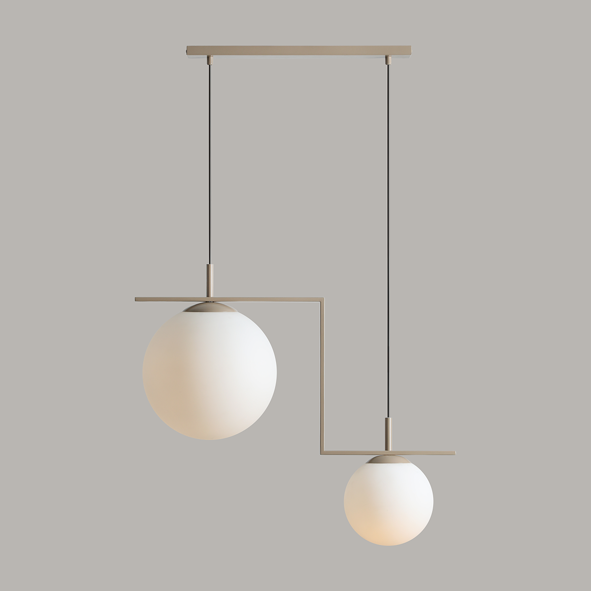 Beżowa lampa wisząca Zac II z dwoma kulistymi kloszami z matowego szkła, zawieszona na cienkich czarnych linkach. Kształt asymetryczny, metalowa konstrukcja w kolorze beżowym, idealna do nowoczesnych wnętrz.