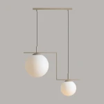 Beżowa lampa wisząca Zac II z dwoma kulistymi kloszami z matowego szkła, zawieszona na cienkich czarnych linkach. Kształt asymetryczny, metalowa konstrukcja w kolorze beżowym, idealna do nowoczesnych wnętrz.