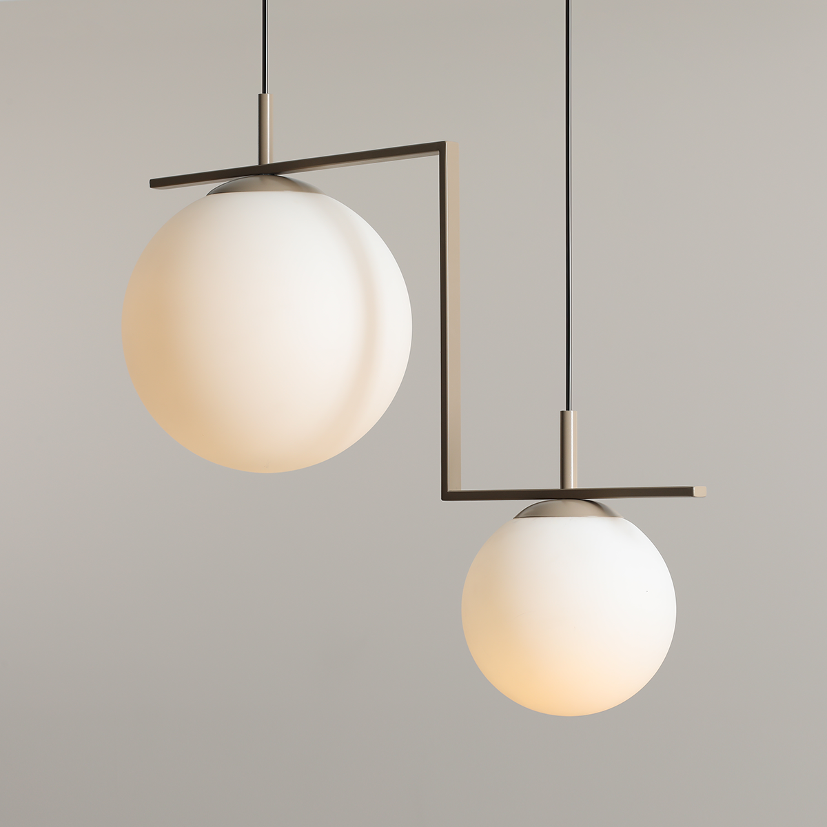 Beżowa lampa wisząca Zac II z dwoma kulistymi kloszami z matowego szkła, zawieszona na minimalistycznym ramieniu. Klosze różnej wielkości, umieszczone w asymetrycznej konfiguracji, na czarnym przewodzie. Tło w jasnym odcieniu.
