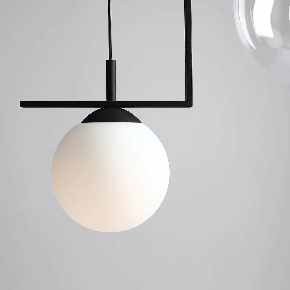 Lampa wisząca Zac 2-punktowa w kolorze czarnym. Posiada okrągły klosz z matowego szkła w białym kolorze, zawieszony na minimalistycznym, prostym stelażu. Ujęcie zbliżeniowe, ukazujące detale konstrukcji i teksturę klosza. Tło jasnoszare.