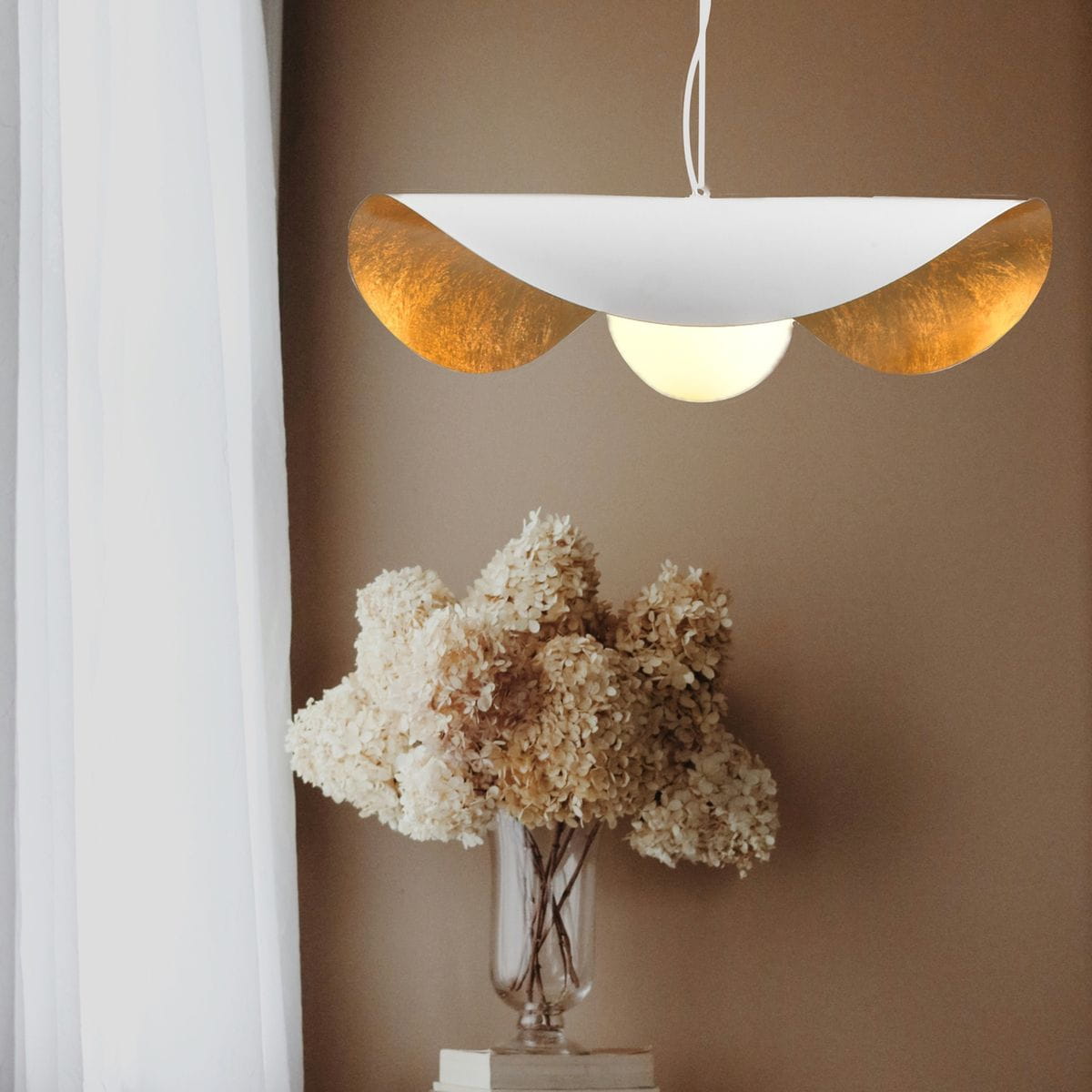 Lampa wisząca Enzo D40 w kolorze białym z złotymi akcentami, z okrągłym źródłem światła na środku. Ujęcie z przodu, zawieszona pod sufitem, w tle dekoracyjne kwiaty w wazonie.