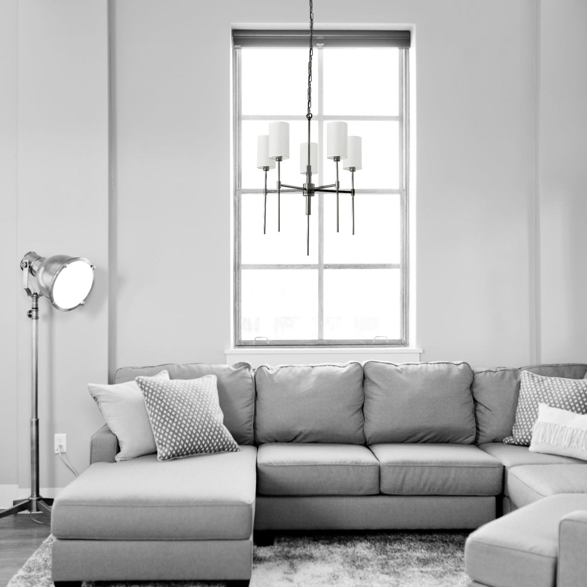 Czarna lampa wisząca Darling z pięcioma kloszami E14, zawieszona na delikatnym łańcuchu. Prosty, elegancki design, umieszczona nad narożnikiem szarej sofy w jasnym wnętrzu.