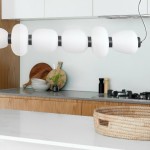 Lampa wisząca Brilla LED w czarnym kolorze z sześcioma białymi kloszami o okrągłym kształcie, zawieszona nad stołem w kuchni. Klosze mają matową fakturę, a lampa emituje światło o temperaturze 3000K. W tle drewniane półki i akcesoria kuchenne.