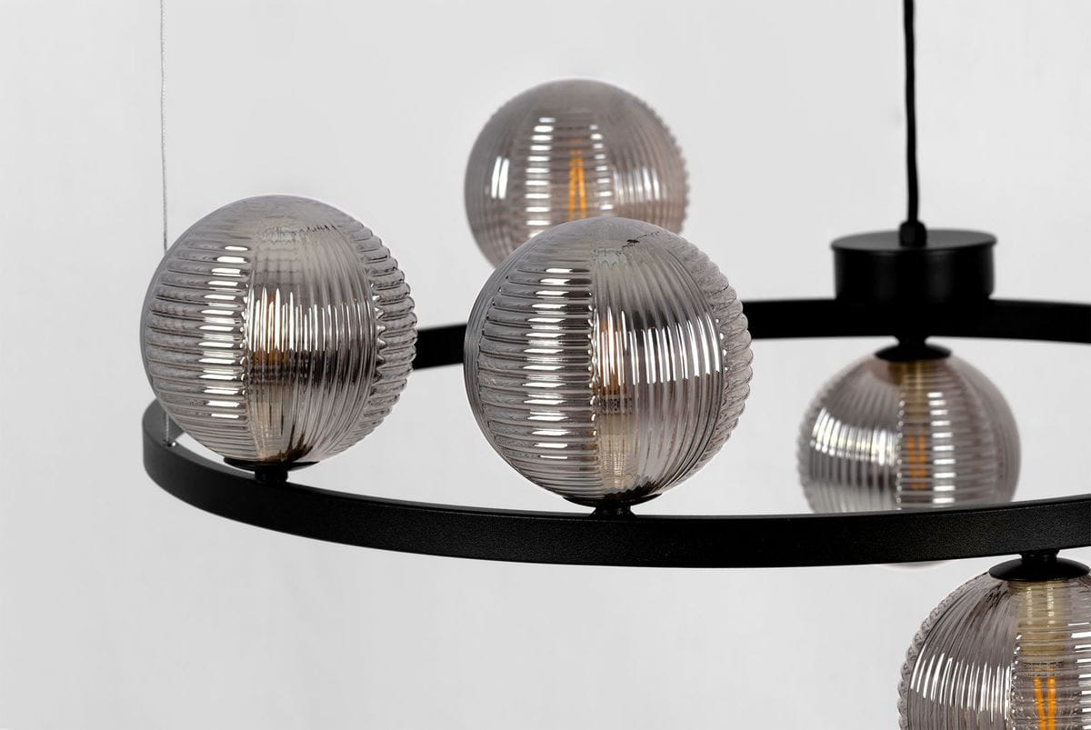 Lampa wisząca Monza z sześcioma oprawami G9, czarna z grafitowym wykończeniem. Okrągła konstrukcja z metalowym pierścieniem, na którym zawieszone są przezroczyste, żłobkowane klosze. Ujęcie z góry, eksponujące detale kloszy i ich rozmieszczenie.