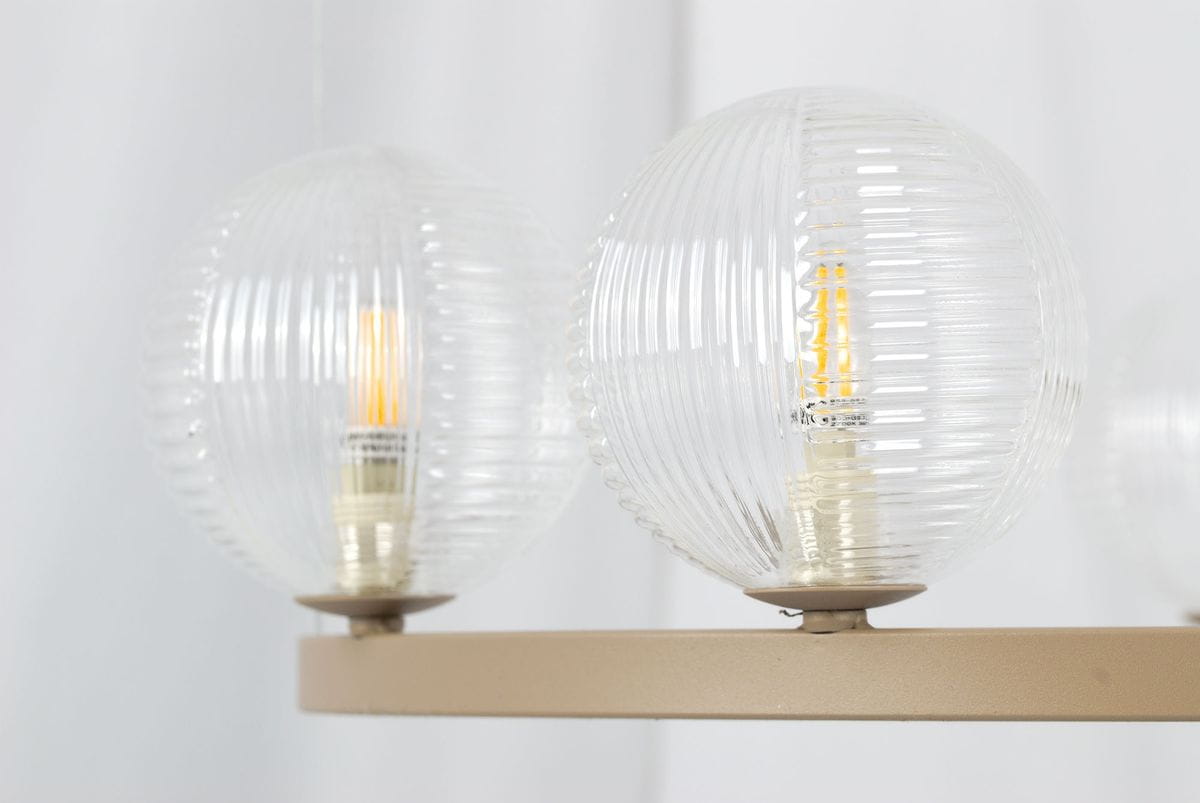Lampa wisząca Tesoro 6xG9 w kolorze beżowym z przezroczystymi, żebrowanymi kloszami. Ujęcie z boku, ukazujące dwa klosze z widocznymi żarówkami. Metalowa podstawa w odcieniu beżowym. Tło jasne, minimalistyczne.