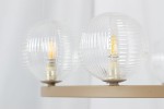 Lampa wisząca Tesoro 6xG9 w kolorze beżowym z przezroczystymi, żebrowanymi kloszami. Ujęcie z boku, ukazujące dwa klosze z widocznymi żarówkami. Metalowa podstawa w odcieniu beżowym. Tło jasne, minimalistyczne.