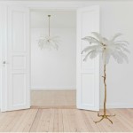 Lampa wisząca Emu 6xE14 w kolorze złotym i białym, o kształcie przypominającym pióra, zawieszona na długim przewodzie. W tle widoczny stół z podłogą drewnianą oraz otwarte drzwi.