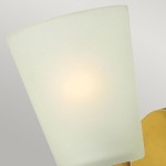 Kinkiet Zelda 1xE27 w kolorze złotym mosiądzu. Lampa ma matową, lekko zaokrągloną osłonę w białym kolorze, która rozprasza światło. Ujęcie z bliska, pokazujące detal klosza oraz elementy mocujące. Tło w stonowanych odcieniach szarości.