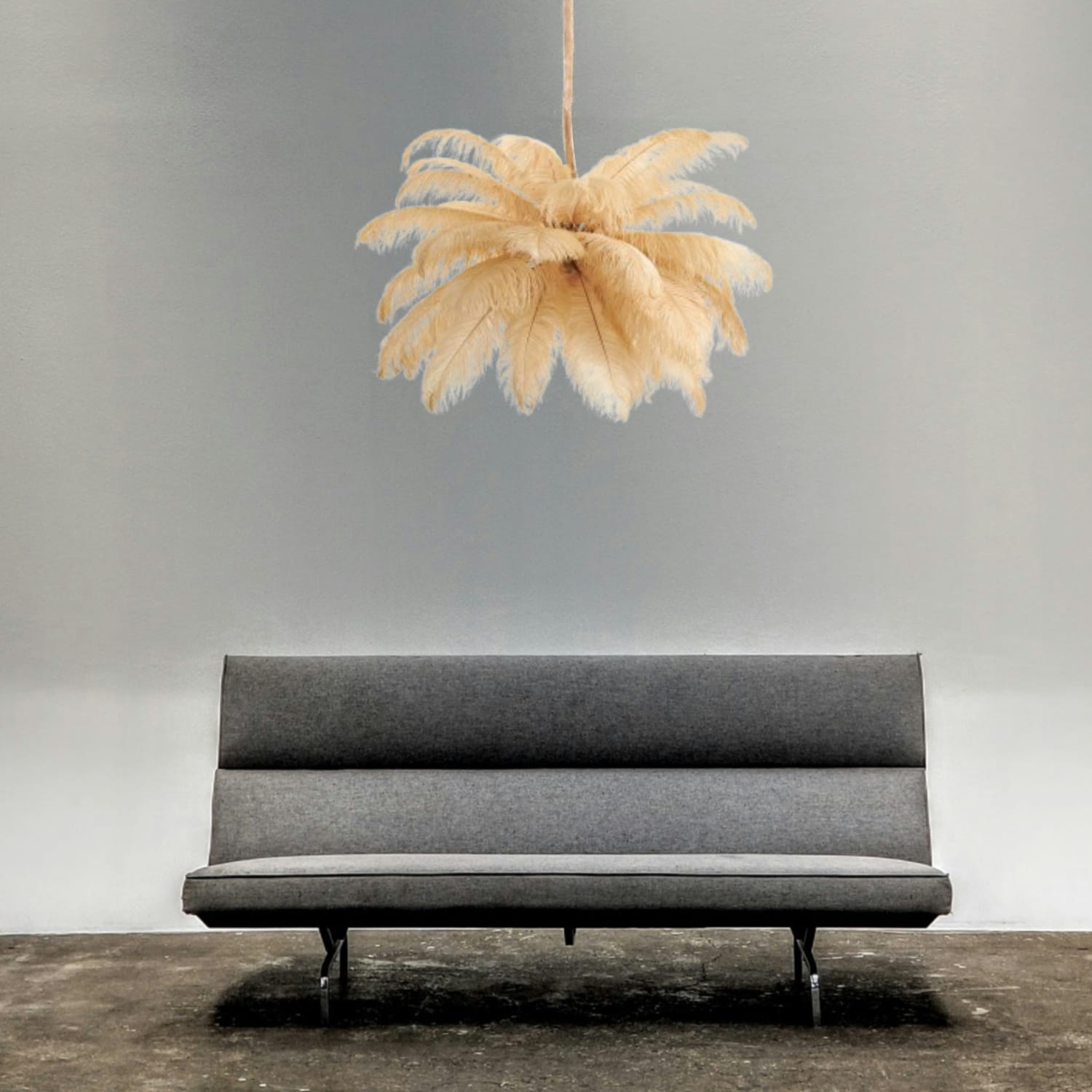 Lampa wisząca Emu w kolorze złotym i beżowym, z 6 miejscami na żarówki E14, o formie przypominającej pióra. Zawieszona nad szarym sofą, w minimalistycznym wnętrzu z gładką ścianą. Wykonana z lekkiego materiału, dekoracyjna i nowoczesna.