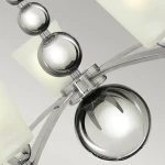 Lampa wisząca Zelda z pięcioma źródłami światła E27, wykonana z polerowanego niklu. Elementy szklane w kształcie kul i prostokątów, błyszcząca powierzchnia oraz nowoczesny design. Ujęcie z bliska, ukazujące detale konstrukcji.