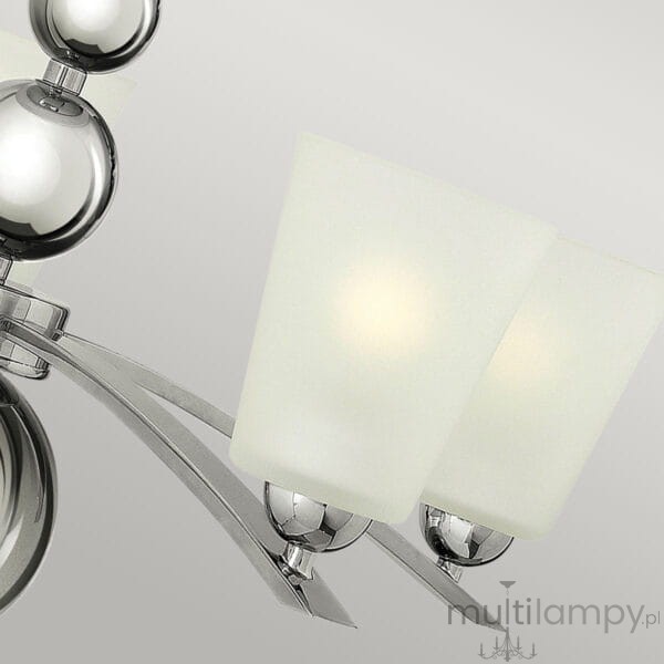 Lampa wisząca Zelda w kolorze polerowanego niklu z pięcioma kloszami z matowego szkła, umieszczona na metalowej konstrukcji. Widoczne zaokrąglone elementy i eleganckie detale. Klosze skierowane w dół, zamontowane na łukowatych ramionach.