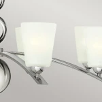 Lampa wisząca Zelda, wykonana z polerowanego niklu, z ośmioma kloszami w kształcie prostokątnym z matowego szkła. Produkt zawieszony na stylowych, zakrzywionych ramionach. Tło w neutralnym odcieniu, co podkreśla elegancję lampy.
