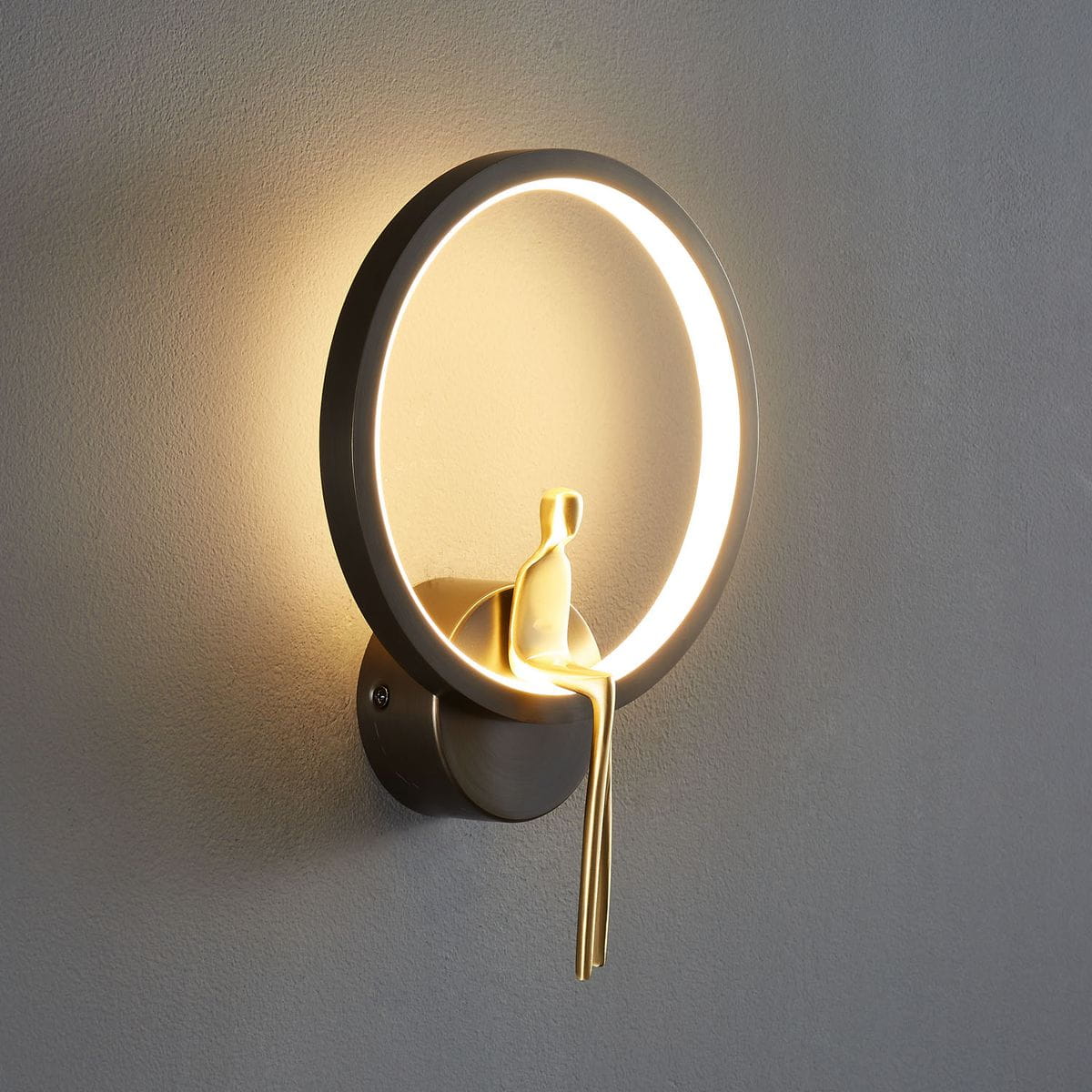 Kinkiet Amici 1xLED/10W w czarnej obudowie z mosiężnym detalem. Okrągła lampa z podświetleniem LED i figurką, umieszczona na ścianie. Widok z boku, podkreślający elegancki design i unikalny kształt.