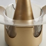 Lampa stołowa Block w kolorze złotym z kloszem z przezroczystego szkła. Ujęcie z góry, ukazujące stożkowaty kształt podstawy oraz detale wykończenia. Widoczny gwint E27 do żarówki. Tło jednolite, jasne.