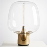 Lampa stołowa Block z metalową podstawą w kolorze złotym i przezroczystym kloszem. Źródło światła E27 w centralnej części. Ujęcie frontalne, produkt stoi na białym tle, bez dodatkowych elementów.