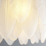 Lampa wisząca Piuma z 10 miejscami na żarówki E14, wykonana z mosiądzu. Osłona lampy zdobiona białymi, teksturowanymi liśćmi, emitującymi miękkie światło. Ujęcie zbliżeniowe na detale liści i źródło światła.
