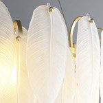 Lampa wisząca Piuma z mosiądzu, z 10 kloszami w kształcie przezroczystych liści. Klosze mają delikatną fakturę, zamocowane na okrągłej konstrukcji. Widoczna ciepła iluminacja od wewnątrz. Ujęcie z bliska, ukazujące szczegóły materiału.