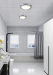 Plafon Condus IP44 z jedną oprawą E27 w chromowanej obudowie, zamontowany na suficie w łazience. Produkt z białym, okrągłym kloszem, w nowoczesnym stylu, w otoczeniu jasnych płytek i białych mebli.
