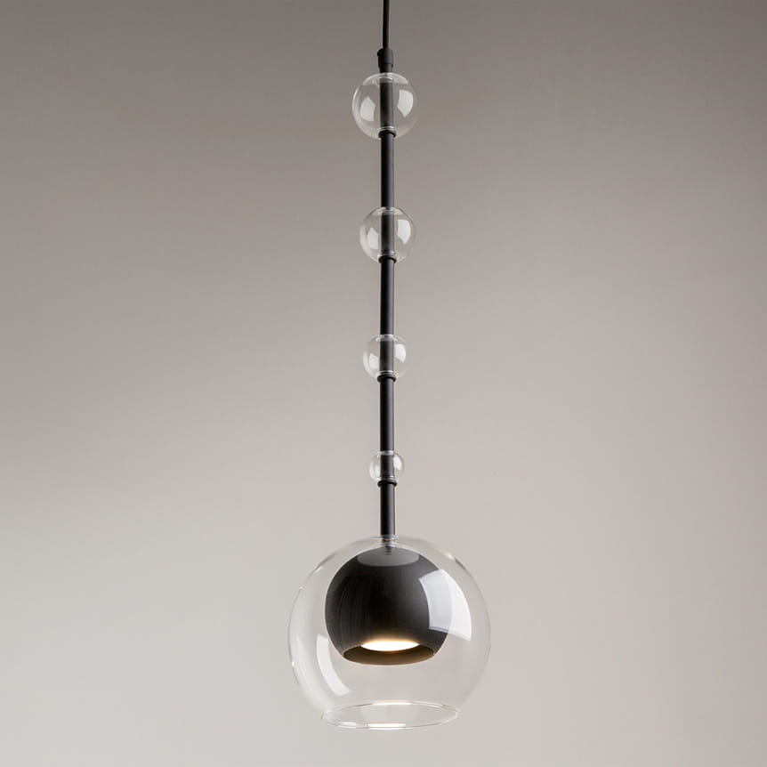 Lampa wisząca Ross z jedną żarówką GU10, czarna podstawa z transparentnym kloszem w kształcie kuli. Produkt zawieszony na cienkim, czarnym przewodzie, z dekoracyjnymi, szklanymi kulkami na osi. W tle jednolite, jasne.