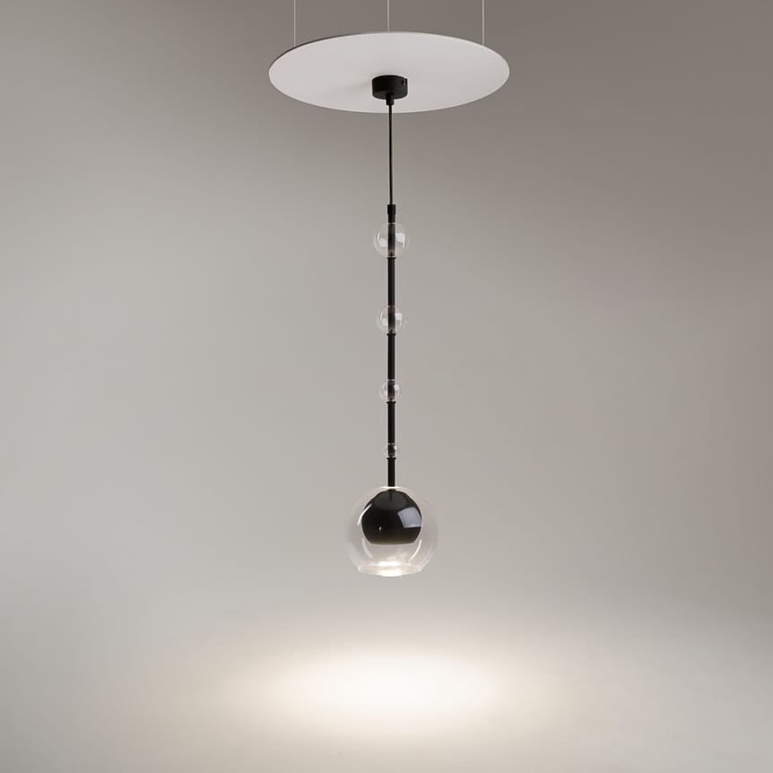 Lampa wisząca Ross z jednym gniazdem GU10, czarna z przezroczystym kloszem. Posiada okrągłą podsufitkę oraz wiszący, cienki przewód z trzema przezroczystymi elementami. Produkt wisi pionowo, emitując światło w dół na jasnym tle.