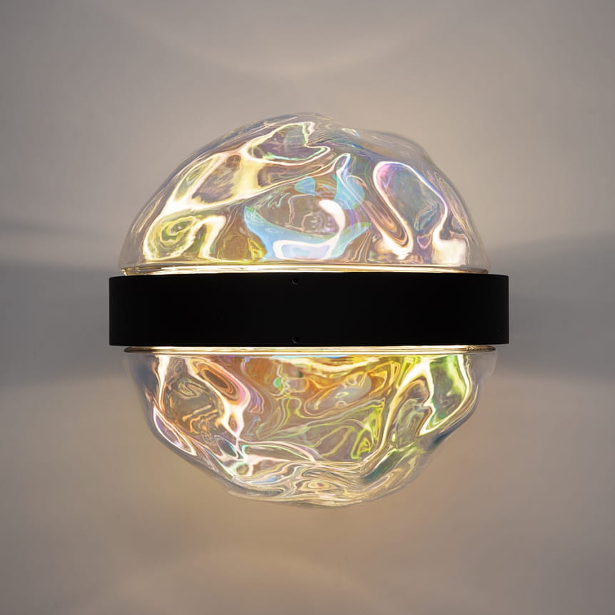 Kinkiet LED Misterio w kolorze czarnym z przezroczystym kloszem o falistej fakturze, emitujący ciepłe światło (2700K). Produkt zamontowany na ścianie, widoczny z przodu, z centralnym czarnym paskiem. Idealny do nowoczesnych wnętrz.