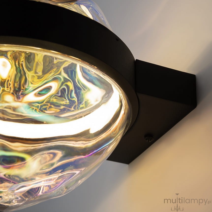 Lampa wisząca LED Misterio, czarna, z przezroczystą, kulistą oprawą, emitująca ciepłe światło o temperaturze 2700K. Zainstalowana na ścianie, z widocznym detalem zamocowania i refleksami kolorów w szkle.