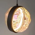 Lampa wisząca LED Misterio w kolorze czarnym, z okrągłym kloszem o przezroczystej, falistej strukturze, emitującym ciepłe światło (2700K). Klosz osadzony na metalowej podstawie z delikatnym złotym detalem. Zawieszona na czarnym przewodzie.