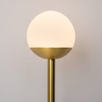 Kinkiet LED w kolorze mosiądzu z okrągłą, białą kloszem, umieszczony na prostym, cylindrycznym stelażu. Klosz ma matowe wykończenie, a lampa emituje ciepłe światło (3000K). Ujęcie frontalne, na jasnym tle.