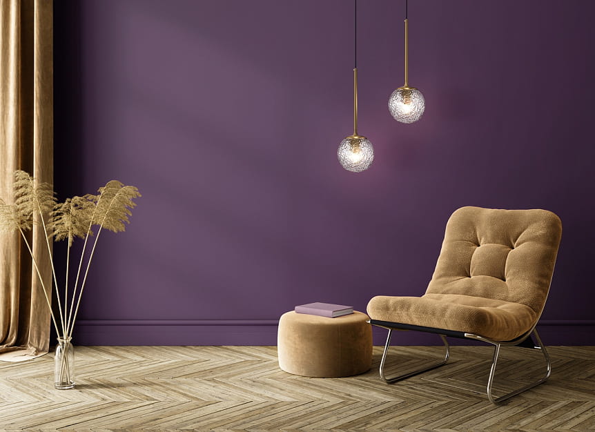 Lampa wisząca Ligero 1xE27 w mosiężnej oprawie, z przezroczystymi kloszami w kształcie kul, zawieszona na czarnych przewodach. Ujęcie z boku, w tle fioletowa ściana, obok beżowy fotel i pufa, dekoracyjne rośliny w wazonie.