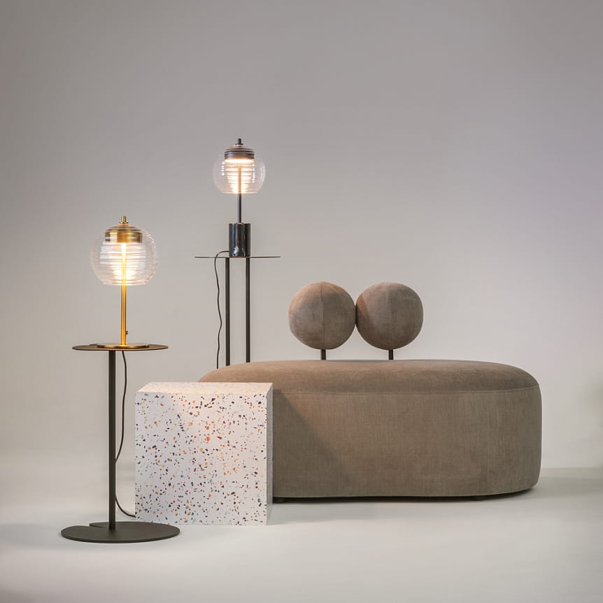 Czarna lampa stołowa LED Mystic o mocy 8W i temperaturze barwowej 3000K, stojąca na okrągłej podstawie. W tle widoczna kanapa z poduszkami w kształcie kul, obok biały stolik z kolorowymi akcentami.