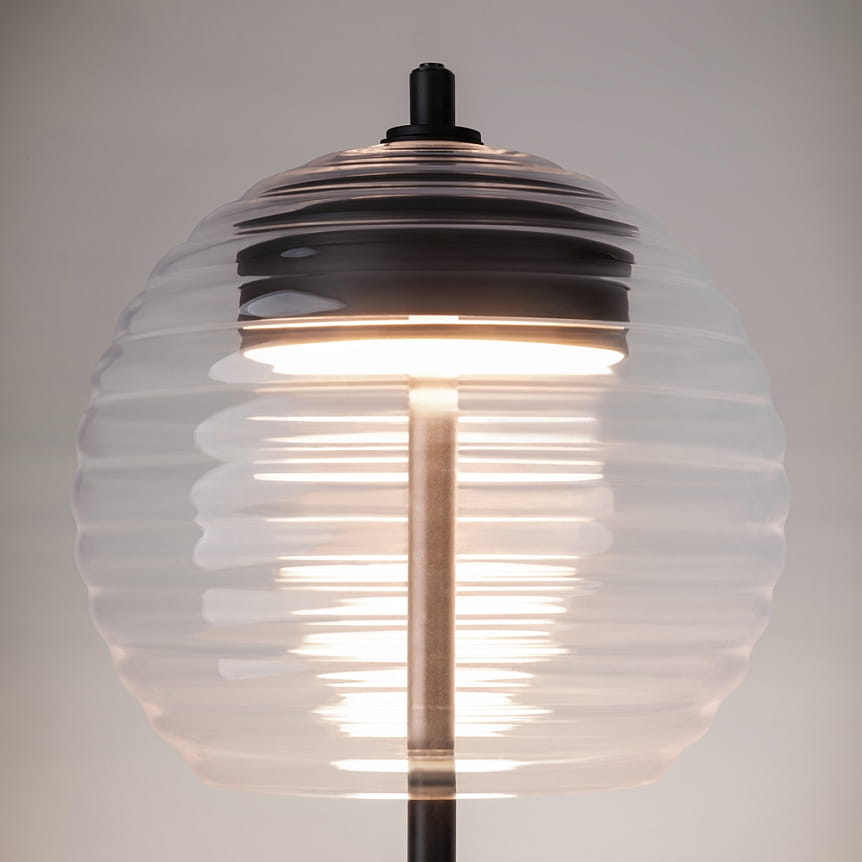 Lampa stołowa LED Mystic o mocy 8W i temperaturze barwowej 3000K. Czarna podstawa z metalowym wykończeniem. Szklany klosz w kształcie kuli z delikatnym, falistym wzorem. Ujęcie z góry, ukazujące źródło światła.