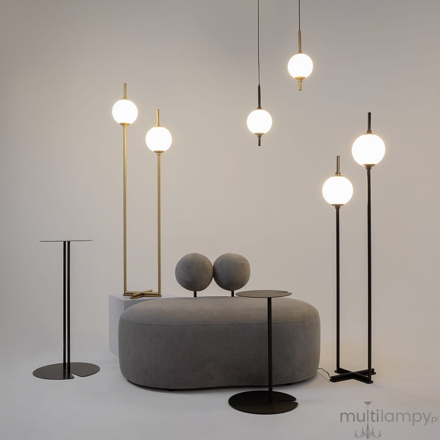 Lampa wisząca LED The Sixth Sense o mocy 7W i barwie 3000K w kolorze mosiądzu. Produkt zawieszony w grupie z lampami podłogowymi, w nowoczesnym wnętrzu z szarym, zaokrąglonym sofą i stolikami w kolorze czarnym. Tło proste, neutralne.