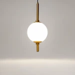 Lampa wisząca LED The Sixth Sense, 7W, 3000K w kolorze mosiądzu. Okrągła, mleczna kula umieszczona na mosiężnym uchwycie, zawieszona na cienkim przewodzie, w minimalistycznym stylu. Tło jasne, jednolite.