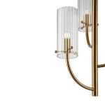 Lampa wisząca Arco z trzema źródłami światła G9, wykonana z mosiądzu. Posiada cylindryczne klosze z przezroczystego szkła z pionowymi żłobieniami. Ujęcie z boku, ukazujące detal konstrukcji i kształt.