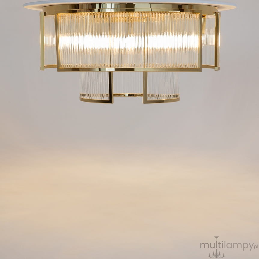 Lampa sufitowa Frame w kolorze złotym, z miejscem na 9 żarówek E14. Okrągła konstrukcja z przezroczystymi, prążkowanymi elementami. Ujęcie frontalne, wisząca w centralnej pozycji, na jasnym tle.