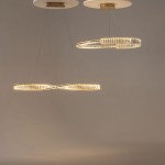 Lampa wisząca LED Krone w kolorze mosiądzu, o mocy 45W i temperaturze barwowej 3000K. Posiada dwa pierścienie: jeden okrągły, drugi w kształcie fali, zawieszone na cienkich linkach, z subtelnym podświetleniem. Tło jasnoszare.