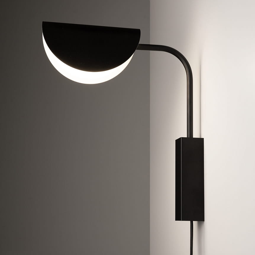 Kinkiet Mollis 1-punktowy w kolorze czarnym, z okrągłym kloszem w kształcie półksiężyca, zamontowany na ścianie. Lampa ma prosty, minimalistyczny design z metalowym ramieniem i prostokątną podstawą. Oświetlenie skierowane w dół.
