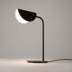 Czarna lampa stołowa Mollis z 1 punktem świetlnym, z metalowym, zaokrąglonym kloszem i smukłym, prostym ramieniem. Ujęcie z boku, na jasnym tle, ukazujące podstawę oraz kabel.