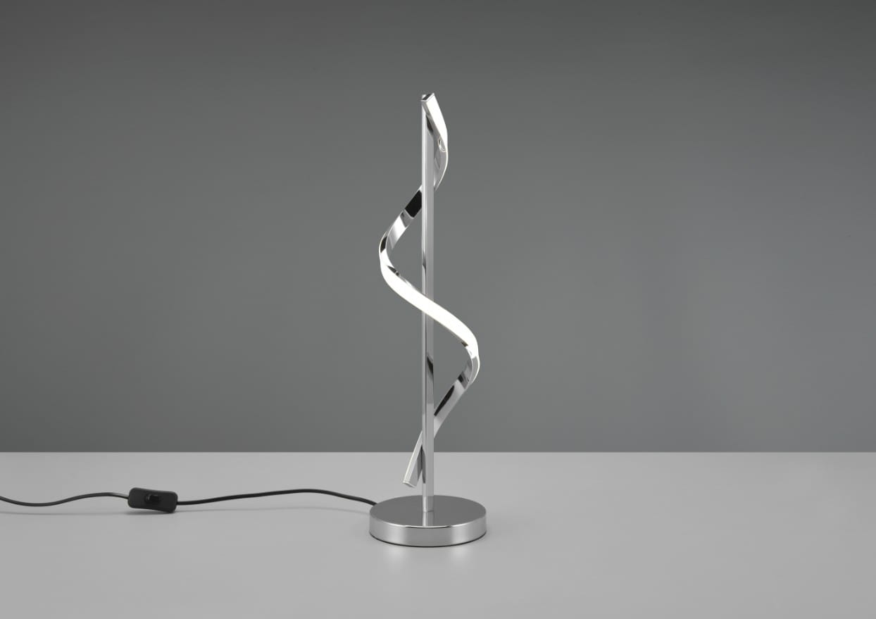 Isabel LED lampa stołowa 1-punktowa w chromowanej obudowie, z falującym kształtem. Produkt stoi na okrągłej, metalowej podstawie. Widoczny czarny przewód z włącznikiem. Tło w odcieniach szarości.