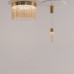 Lampa wisząca LED w złotym kolorze, z okrągłym kloszem ozdobionym cienkimi złotymi frędzlami. Posiada długi, smukły zwis z cylindrycznym źródłem światła. Ujęcie z przodu na jasnym tle, ukazujące elegancki design.