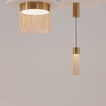 Lampa wisząca LED Imaginary w kolorze złotym, z głównym kloszem w formie cylindrycznej z frędzlami oraz mniejszym, prostym kloszem. Oświetlenie ma moc 5W i temperaturę barwową 3000K, zawieszona na cienkim przewodzie, z jasnym tłem.