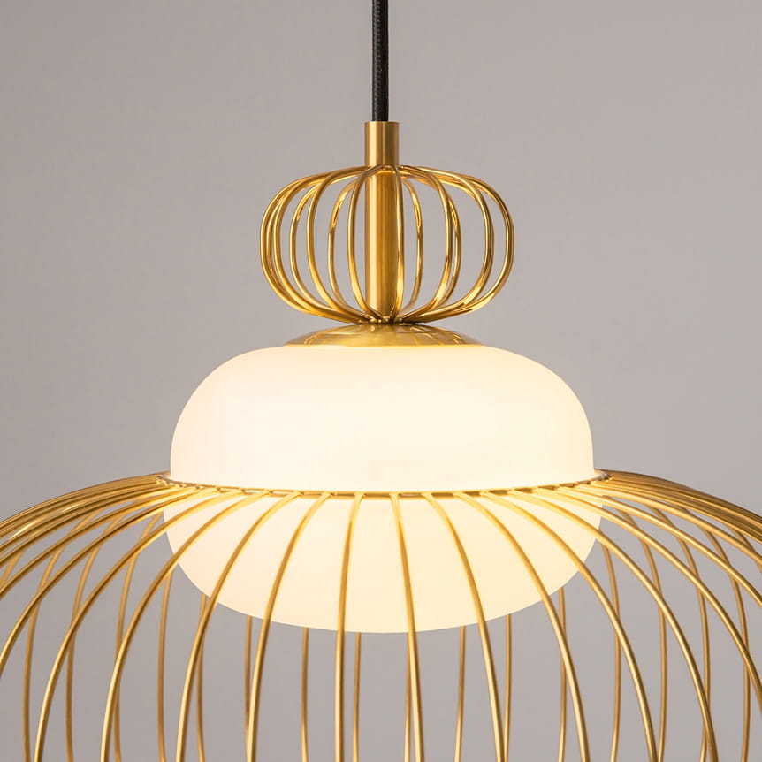 Lampa wisząca Levitation 1xG9 z mosiądzu, z okrągłym kloszem z białego szkła, otoczonym złotą, metalową siatką. Ujęcie z boku, pokazujące detal konstrukcji oraz zawieszenie. Tło jasne, neutralne.
