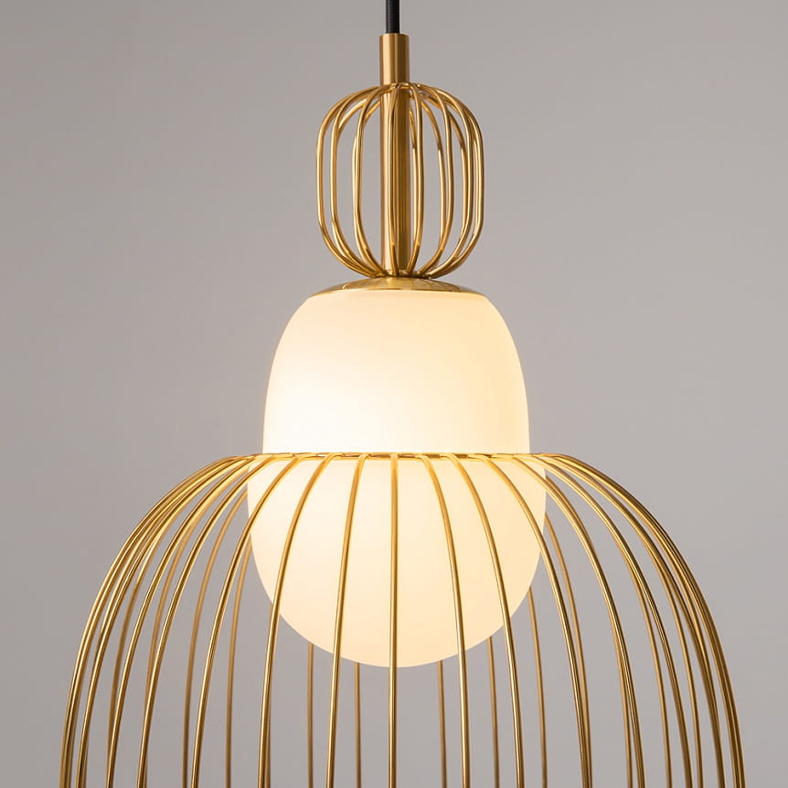 Lampa wisząca Levitation w kolorze mosiądzu z białym kloszem. Okrągły, matowy klosz otoczony jest metalową, ażurową konstrukcją. Ujęcie z góry, pokazujące detal wykończenia i kształt lampy. Zawieszona na czarnym kablu.