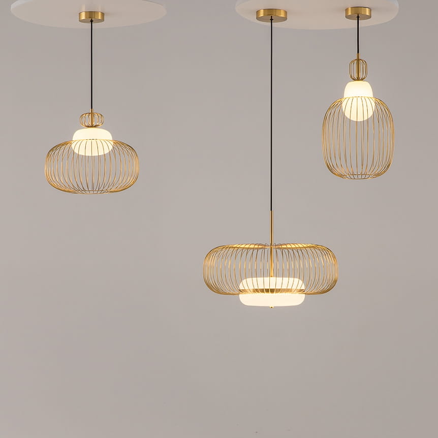 Lampa wisząca Levitation 1xG9 w kolorze mosiądzu, składająca się z trzech elementów o różnym kształcie. Konstrukcja z cienkich metalowych prętów, w centralnej części biała oprawa, zawieszona na czarnych przewodach. Tło jasne.