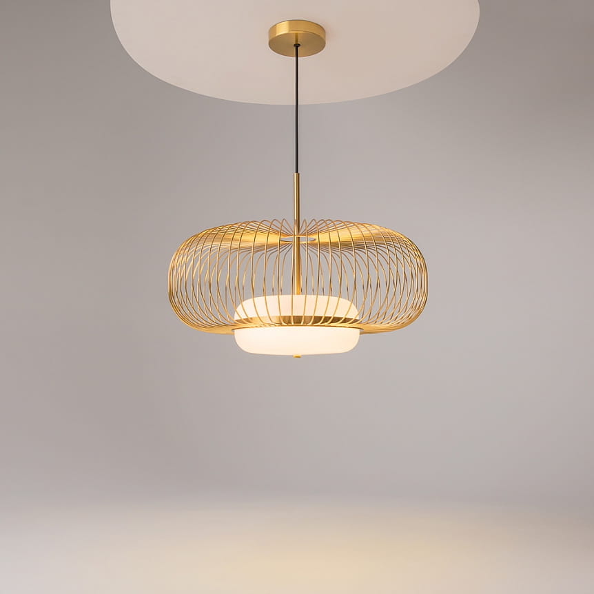 Lampa wisząca Levitation 1xG9 w kolorze mosiądzu z metalowym kloszem w formie ażurowej siatki. Ułożona na długim przewodzie, z białym, okrągłym elementem u podstawy, na tle szarej ściany.