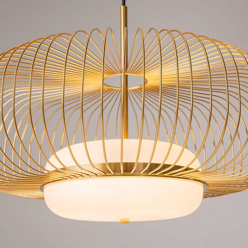 Lampa wisząca Levitation 1xG9 w kolorze mosiężnym. Okrągła, metalowa konstrukcja z delikatnymi, spiralnymi prętami. U podstawy znajduje się mlecznobiały klosz. Ujęcie z bliska, podkreślające detale oraz nowoczesny design.