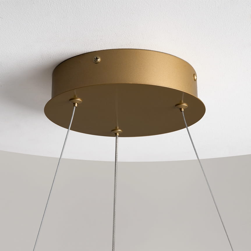 Mosiężny uchwyt lampy wiszącej Curve LED z dwoma stalowymi linkami. Uchwyt ma okrągły kształt i gładką, matową powierzchnię. Widoczny jest sufit, na którym zamontowano lampę.