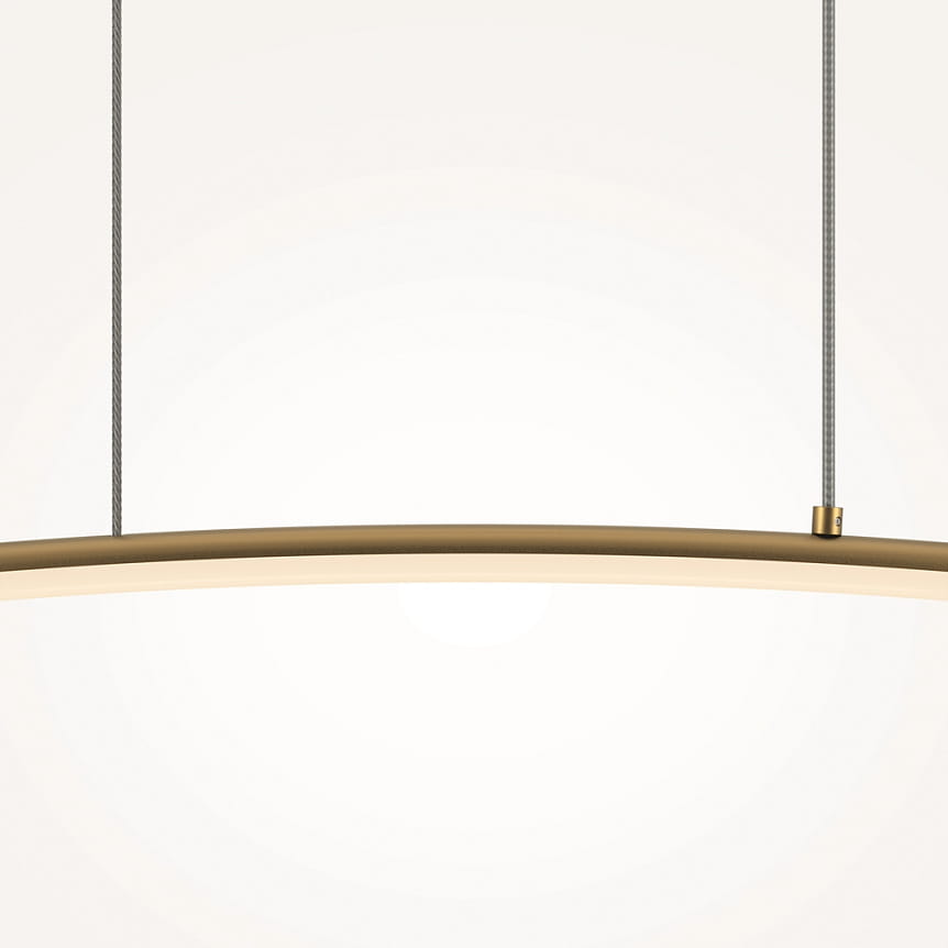 Lampa wisząca LED Curve o mocy 15W, w kolorze mosiądzu, ma elegancki, zakrzywiony kształt. Zawieszona na dwóch cienkich linkach, emituje ciepłe światło. Tło jest jasne, co podkreśla design lampy.